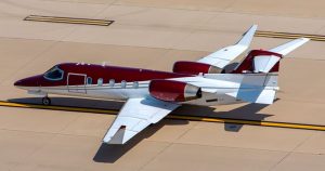 Image of a white and red jet sitting on a cream colored tarmac in the sun