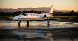 Image of a white with yellow and blue linings jet, reflecting on wet tarmac with mountains in the background