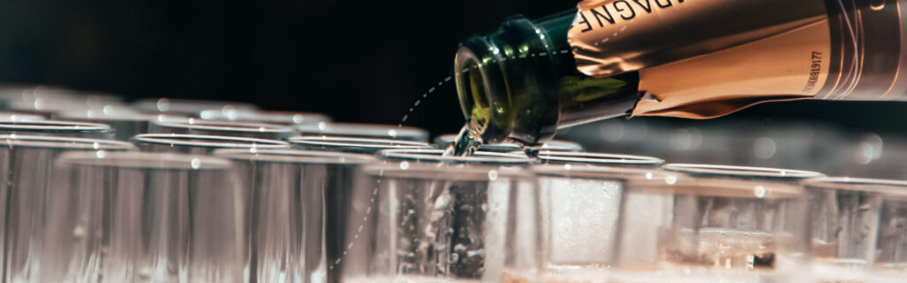 Image of a bottle of champagne being poured into rows of glasses