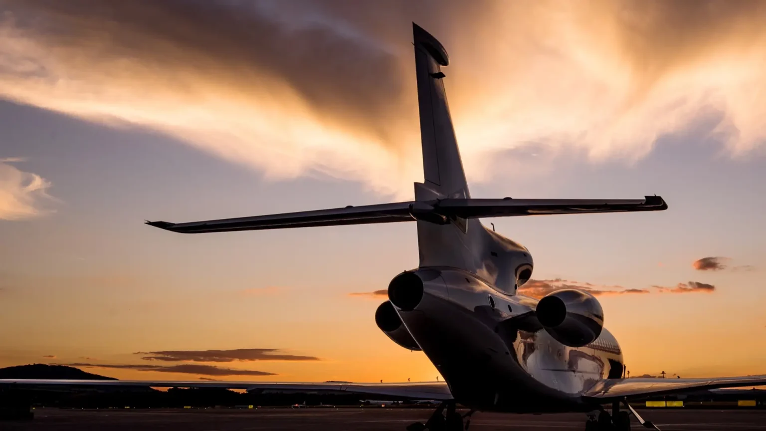 Private jet sitting on tarmac at sunset, rear view.