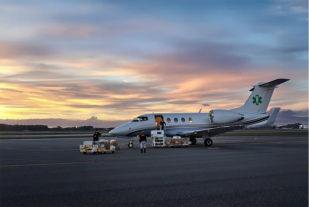 Image of a air ambulance jet on the tarmac with workers filling it, against a sunset backdrop