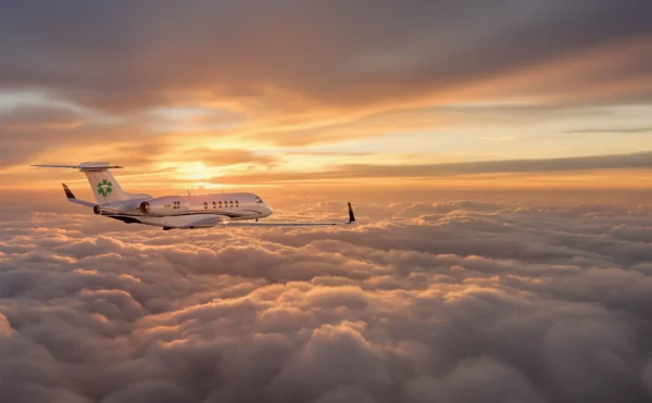 Image of a Avinode Air Ambulance with a green medical sign flying over light clouds into the sunset